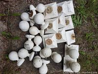Photo showing 23 assorted wooden painted finials including spherical and square base designs placed outdoors on grass and dirt.