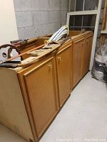 Two plywood lower cabinets stacked against a block wall in a storage area with various tools and hoses on top.