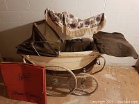 Full view of classic cream-colored English pram with black canopy and floral parasol above, along with red Pram Company box on ground.