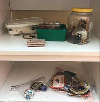 Clear view of various badges and pins in plastic containers and bags on shelf.