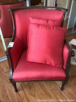 Front angle view of red silk raw wingback chair with matching pillow, showing carved wooden frame and fabric upholstery.