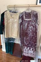 Five women's clothing items hung on a metal rod; visible items include a burgundy East Asian costume dress, cream sleeveless top, and three other garments in darker colors.