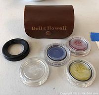 Overview photo showing Bell & Howell brown leather case and four Tiffen lens filters in clear plastic holders, plus black metal filter ring.