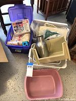 Overview of the lot showing plastic bins with medical and first aid supplies including a metal water jug and storage containers.