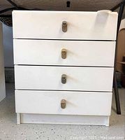 Front view of white melamine chest of drawers showing 4 drawer fronts with metal pull handles and some surface marks.