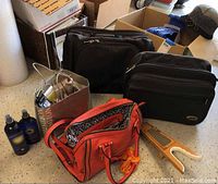 Full lot overview with overnight bags, leather purse, bottles, boot jack, and paper bag of accessories on floor.