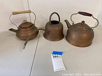Three vintage copper items including two kettles and one watering can on a white table.
