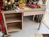 Front angle showing desk with drawer, shelves, and contents on top (contents not included in lot).