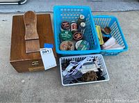 Wooden Kiwi shoe groomer box with attached shoe horn, next to baskets containing shoe polish tins, brushes, cloths, shoe laces, and other shoe care items.