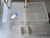 Two clear acrylic display cubes placed side by side on the floor with a small clear magazine rack in front.