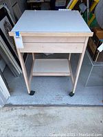 Photo showing the drafting table from the front, highlighting the adjustable white tabletop, drawer, legs, and caster wheels.