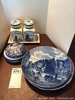Photo showing blue and white Delft decorative plates and jars, candy dish, and additional plates on a wooden surface