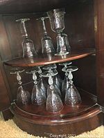 Set of four finely rimmed, delicately etched crystal wine glasses and eight thicker rimmed wine glasses displayed on a wooden shelf inside cabinet.