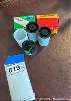 Photo showing five 35mm film rolls including one Kodak Kodachrome ISO 25 in box, one Fujichrome ISO 100 in box, and three additional unboxed rolls with canisters.