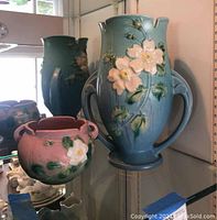 Front view of blue amphora-style vase and pink bowl-style vase on display shelf.