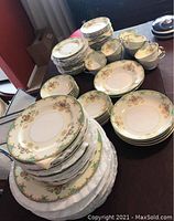 Wide view of the tableware including stacked plates and cups showing floral and gold trim pattern.