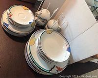 Image showing stacked plates, bowls, and cups with Orbit pattern on a dark wood table.