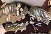 Various Puritan sterling flatware pieces laid out on table, including knives in a roll, forks and spoons on cloth rolls