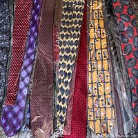 Photo showing approximately 10 silk neck ties in various patterns and colors including purple, burgundy, tan, red, yellow, black, and gray, packed together.