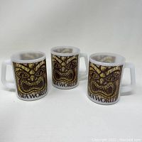 Three vintage Fire King milk glass coffee mugs with Sea World Tiki design arranged in a row.
