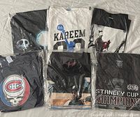 Photo showing six assorted graphic T-shirts with various designs including sports and pop culture.