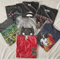 Seven assorted graphic t-shirts arranged on a flat surface, showing variety of designs and colors