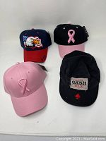 Four baseball caps displayed with eagle, pink ribbons, and Johnny Cash design