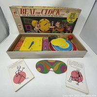 Full view of open game box showing box art, yellow spinner, round colored tokens, cards, and cardboard mask