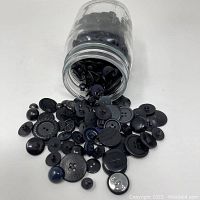 Assorted black and gray buttons spilled out from Ball jar showing different sizes and styles