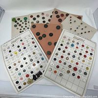 Three button cards displayed overlapping, showing a variety of button types and colors including greens, whites, browns, and reds arranged on cards.