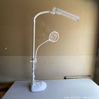 Full view of the white adjustable lamp with top light and attached magnifying glass on a flexible arm.