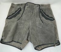 Front view of gray leather lederhosen shorts showing traditional Bavarian style with black scalloped trim on pockets and black piping along edges.