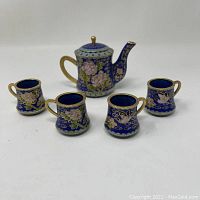 Overview of the miniature cloisonné tea pot and four cups arranged in front of a white background.