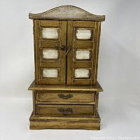 Front view of the miniature wooden dresser jewelry box with closed doors and visible drawer handles.