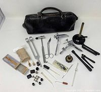 Full view of vintage black leather doctor bag alongside assorted medical instruments spread out showing range of items.