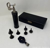 Photo of the ophthalmoscope unit, ear specula, attachments and case exterior on a white surface