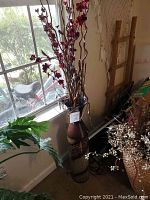 Full view of tall decorative floor vase near window containing artificial red flower twigs and curly branches with string lights.