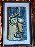 Frontal view of framed abstract folk art panel depicting a stylized face