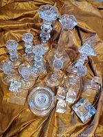 Lot of 18 clear glass candle holders arranged on a gold fabric background showing variety of shapes and sizes, some with faceted stems and bases.