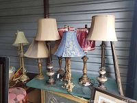 View of all seven table lamps with various fabric shades and ornate metallic bases arranged on a table