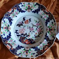 Top view of large scalloped porcelain plate with detailed floral and bird pattern in vivid colors.