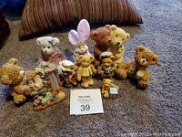 Lot of vintage collectible resin bears and assorted figurines on carpet with striped pillow in background