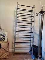 Front view of tall metal rack with multiple horizontal shelves against a wall in a room.