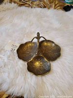 Full view of the tri-compartment brass candy dish showing three leaf-shaped dishes with a central handle, placed on a white fur surface.