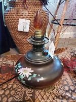 Mid century electric hurricane lamp base with painted flowers and amber flame bulb visible.
