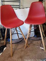 Two red mid-century style molded plastic chairs viewed from the front showing the deep red ergonomic seats and wooden legs.
