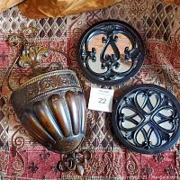 Photo showing the entire lot including one large bronze-tone ornate wall planter and two black decorative wall hooks with scrollwork design on a patterned fabric background.