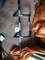 Full view of the pull up bar lying on carpet with orange fabric in the background, showing foam grips and metal frame.