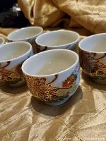 Six Japanese teacups arranged on a golden fabric surface, showing the round shape and outward flared rim.