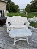 White wicker loveseat with matching table on outdoor deck, showing weathering and wear, angled front view.